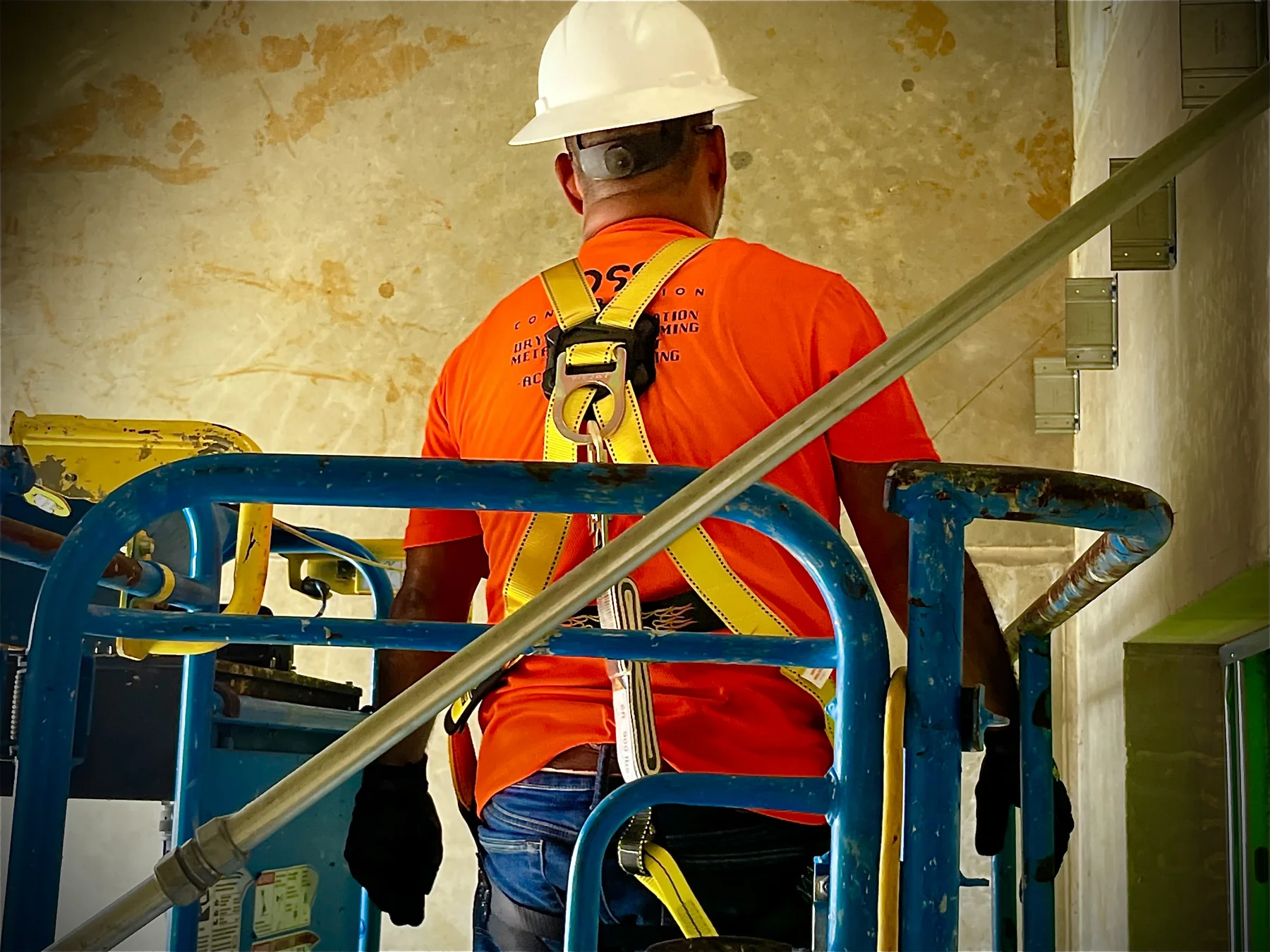 Crew member working from a lift, wearing a hard hat and harness